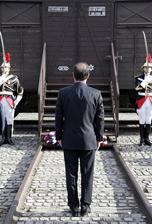 This Sept. 21, 2012, file photo shows French President Francois Hollande standing at attention in front of a train car symbolizing the Drancy camp during the inauguration of the new Shoah memorial in Drancy, a Paris suburb, France. Hundreds of Americans and others deported by France's state rail company SNCF during the Nazi occupation will be entitled to compensation from a $60 million compensation fund that will be financed by France and managed by the United States.